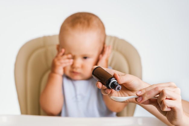 Il bambino non vuole bere la medicina con un cucchiaio e gli afferra la testa. Messa a fuoco selettiva