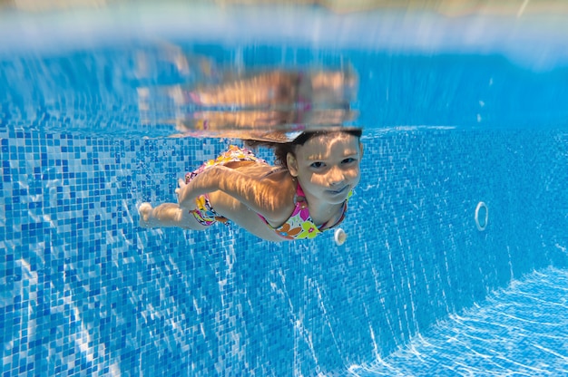 Il bambino nuota in piscina sott'acqua, la ragazza attiva felice si tuffa e si diverte sott'acqua, lo sport per bambini in vacanza con la famiglia