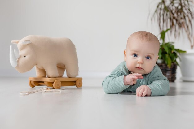 il bambino paffuto in una tuta verde è seduto sul pavimento e gioca con un giocattolo di legno su una corda