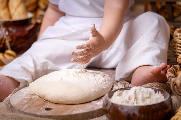 Il bambino piccolo si siede su un tavolo di legno e stende la pasta