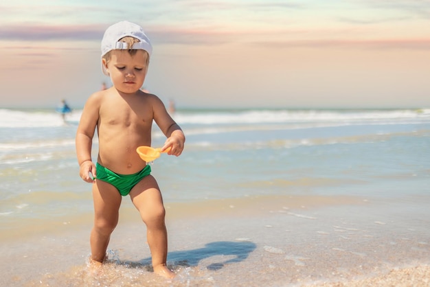 Il bambino raccoglie conchiglie e ciottoli nel mare su un fondo sabbioso sotto il sole estivo in vacanza