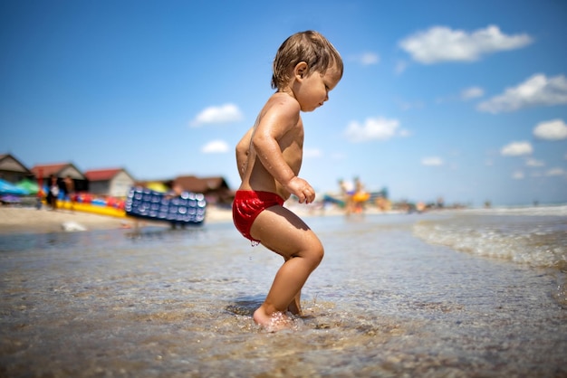 Il bambino raccoglie conchiglie e ciottoli nel mare su un fondo sabbioso sotto il sole estivo in vacanza