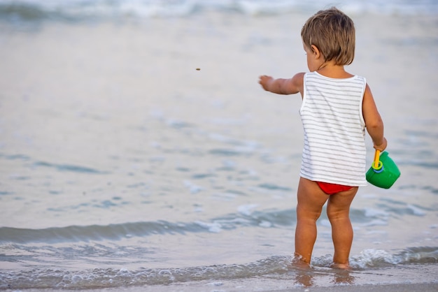 Il bambino raccoglie conchiglie e ciottoli nel mare su un fondo sabbioso sotto il sole estivo in vacanza