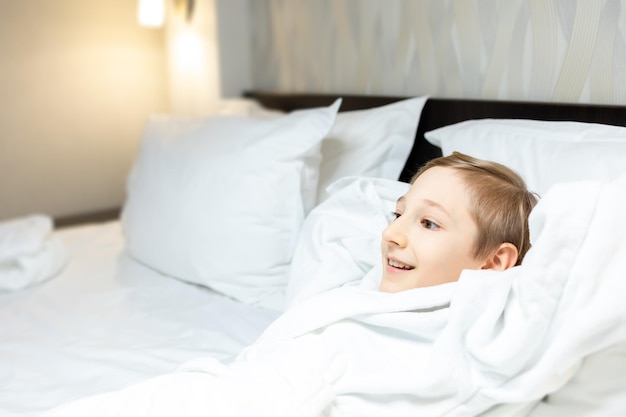 Il bambino riposa su un grande letto in una stanza d'albergo con le mani dietro la testa