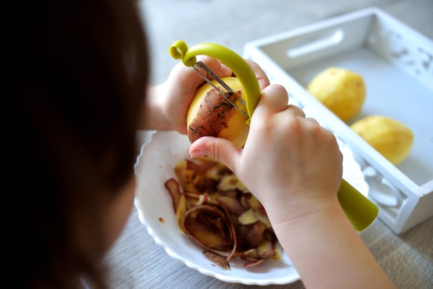 Il bambino sbuccia le patate con un pelapatate verde