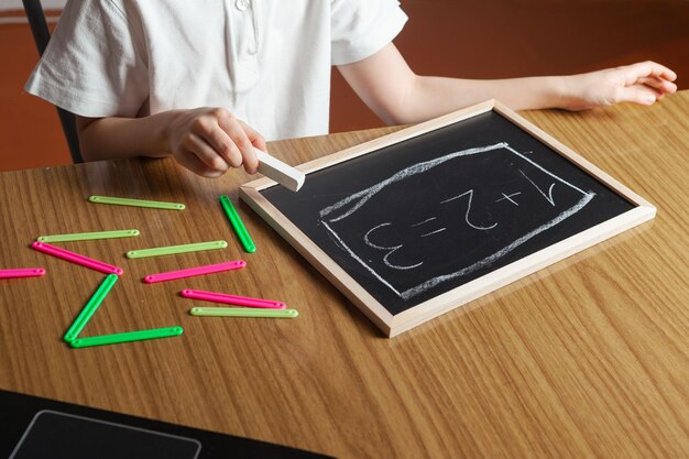 Il bambino scrive i numeri sulla lavagna e conta dai bastoncini colorati della casa.