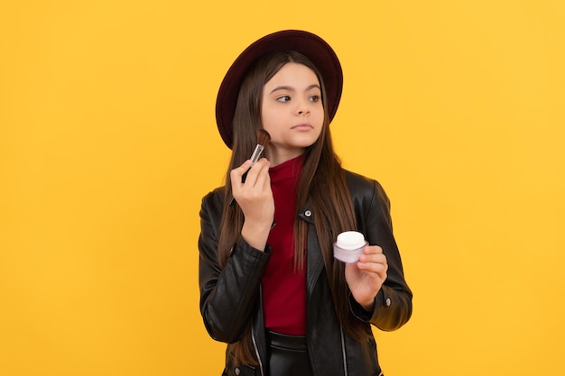 Il bambino serio con il cappello applica la polvere sulla cura della pelle di sfondo giallo