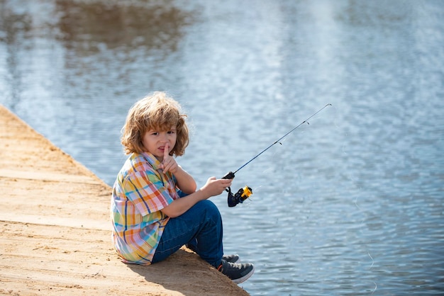 Il bambino serio e piccolo sta pescando sul fiume con una canna da pesca.