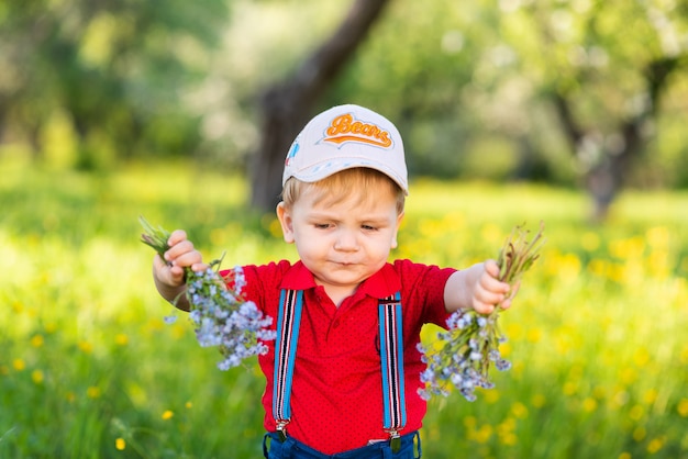 Il bambino si diverte a giocare nella natura tra i fiori e raccoglie un bouquet