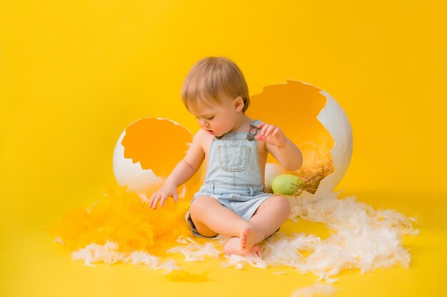 Il bambino si siede con le uova di Pasqua decorative su uno sfondo giallo. il concetto di Pasqua