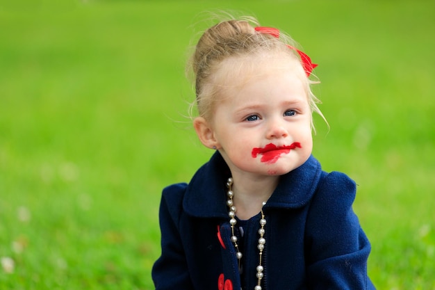 Il bambino si siede e si dipinge le labbra con rossetto rosso