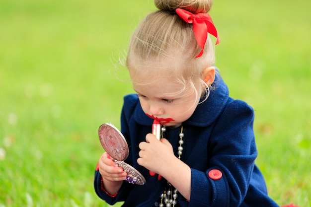 Il bambino si siede e si dipinge le labbra con rossetto rosso