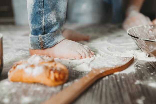 Il bambino si siede sul tavolo e gioca con la farina. piedi del bambino sul primo piano del tavolo.