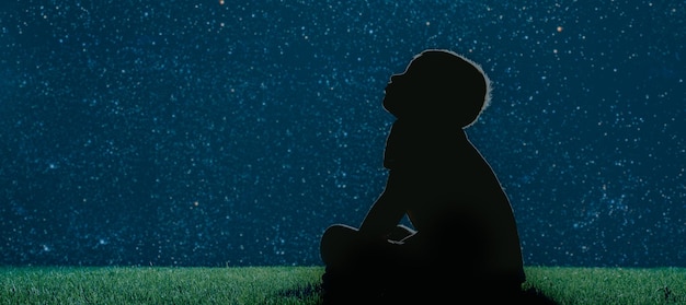 Il bambino si siede sull'erba di notte e guarda il cielo notturno di Natale