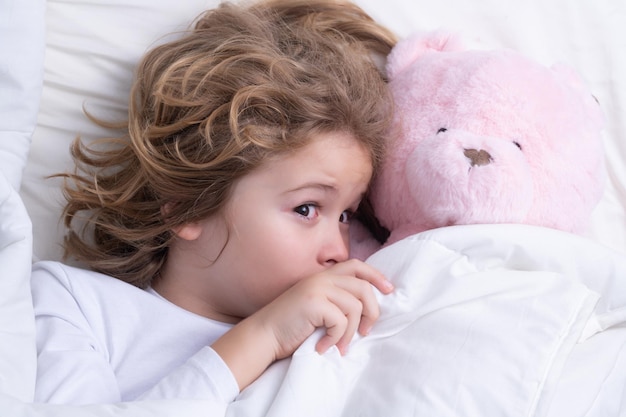 Il bambino si sveglia con un orsacchiotto giocattolo al mattino in camera da letto un ragazzino carino che si sveglia a letto