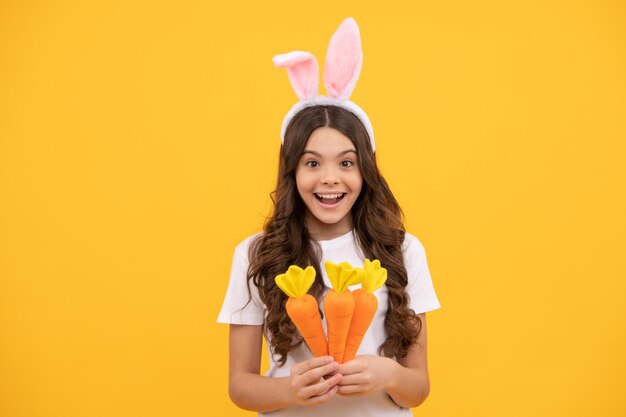 Il bambino sorpreso con le orecchie da coniglio tiene la carota su sfondo giallo pasqua