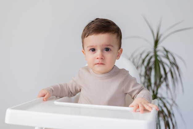 Il bambino sorridente allegro è seduto su un seggiolone bianco per l'alimentazione di alta qualità di sfondo bianco