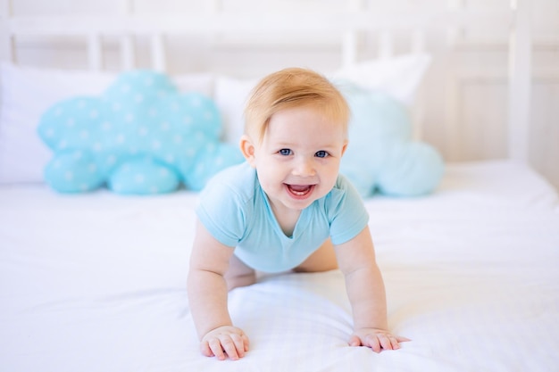 Il bambino sorridente o ridente impara a gattonare sul letto di casa in abiti blu si sveglia la mattina o va a letto felice infanzia e famiglia