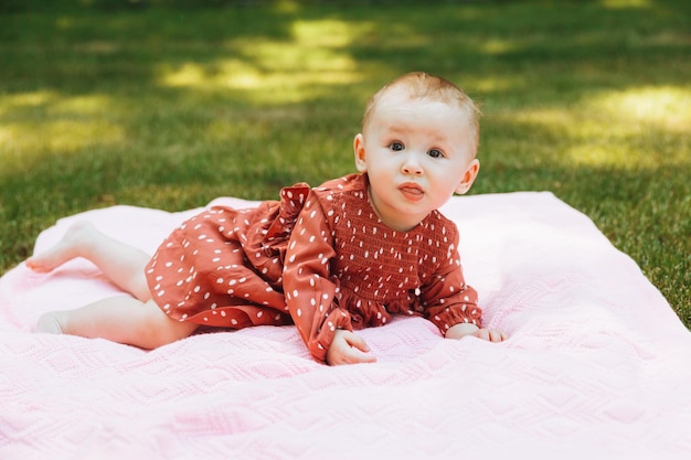 Il bambino sorridente si trova su una coperta sull'erba nel parco bambina di 6 mesi