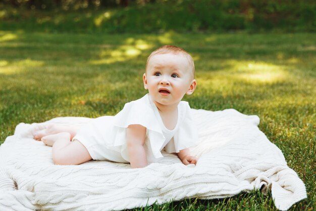 Il bambino sorridente si trova su una coperta sull'erba nel parco bambina di 6 mesi