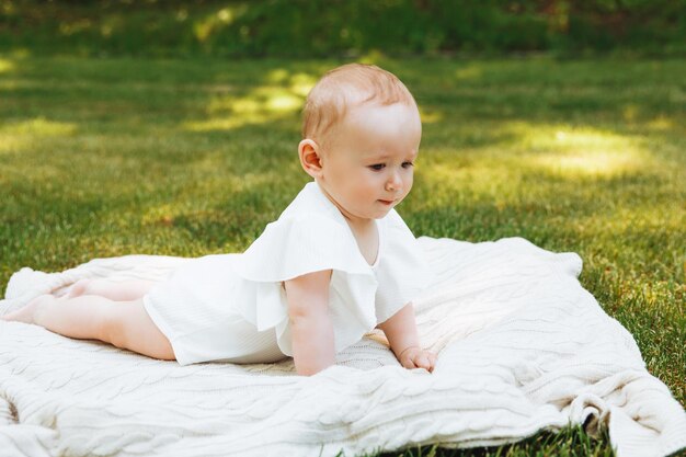 Il bambino sorridente si trova su una coperta sull'erba nel parco bambina di 6 mesi