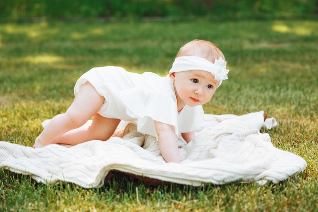 Il bambino sorridente si trova su una coperta sull'erba nel parco bambina di 6 mesi