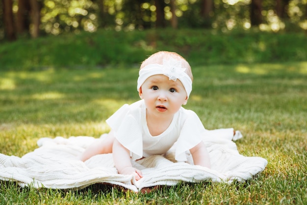 Il bambino sorridente si trova su una coperta sull'erba nel parco bambina di 6 mesi