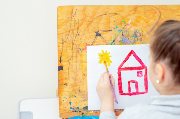 Il bambino sta disegnando il sole giallo con la casa rossa