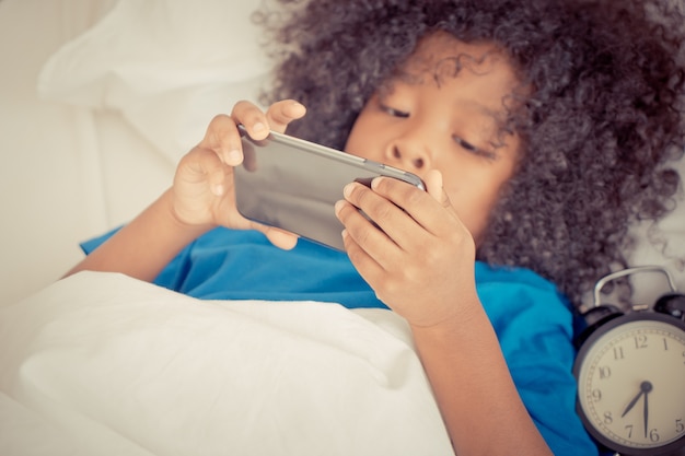 Il bambino sta giocando con il telefono cellulare sul letto con la sveglia