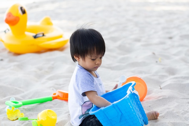 Il bambino sta giocando da solo su una spiaggia bianca con un secchio e una pala di sabbia da vicino