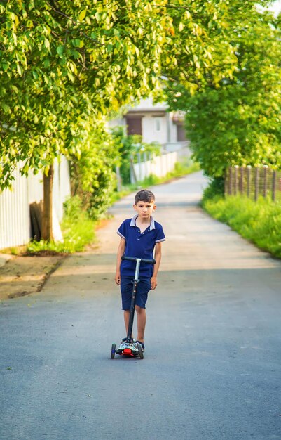 Il bambino sta guidando uno scooter per strada. Messa a fuoco selettiva.