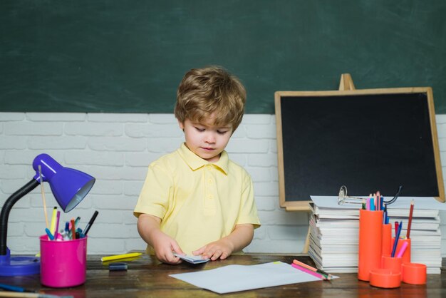 Il bambino sta imparando in classe sullo sfondo della lavagna. I bambini si preparano per la scuola. Ragazza e ragazzo con l'espressione del viso felice vicino alla scrivania con materiale scolastico.