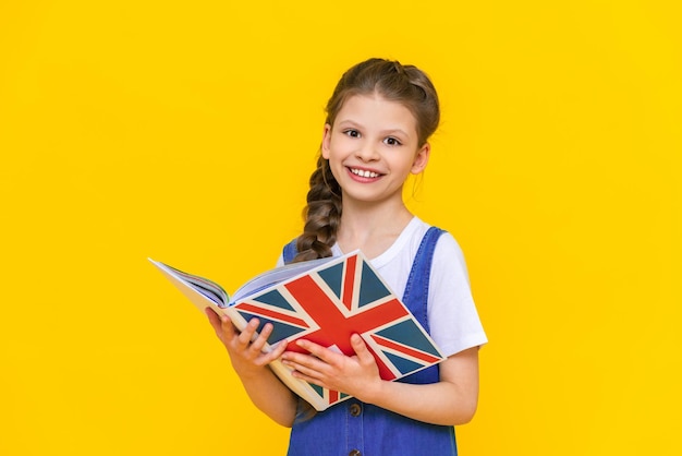 Il bambino sta imparando l'inglese britannico Ritratto di una bambina che tiene un libro Educazione dei bambini Imparare le lingue straniere sfondo giallo isolato