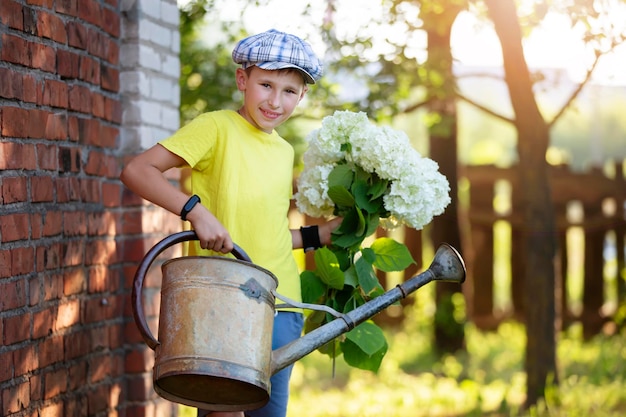 Il bambino sta lavorando in giardino Ragazzo con un annaffiatoio vintage e un mazzo di fiori