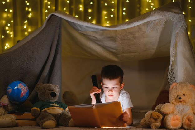 Il bambino sta leggendo un libro con una torcia