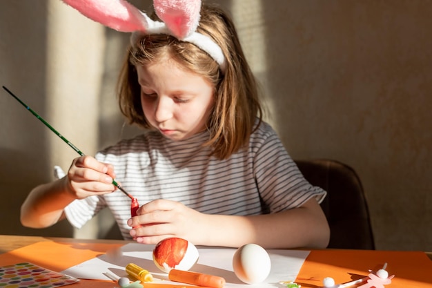 Il bambino sta preparando la decorazione delle uova di pasqua e la ragazza divertente nelle orecchie dei coniglietti di pasqua si prepara