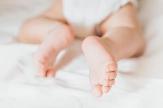 Il bambino striscia su un letto bianco Gambe di un neonato da vicino