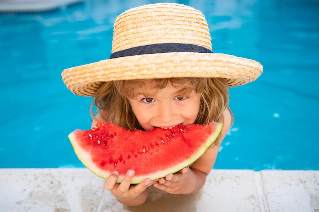 Il bambino stupito e divertente mangia l'anguria vicino alla piscina