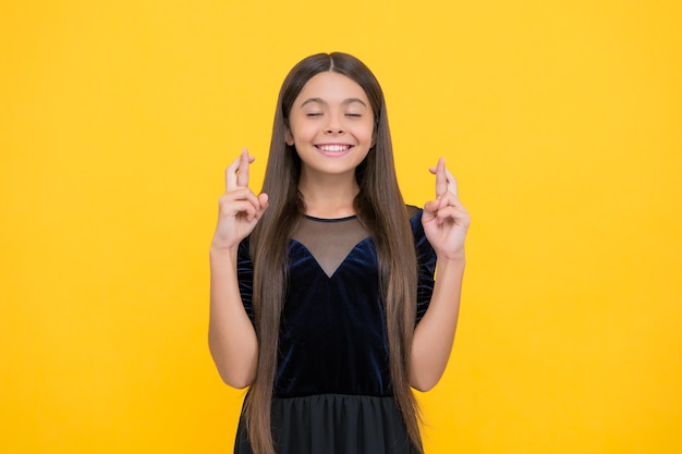 Il bambino superstizioso con lunghi capelli castani in abito alla moda esprime il desiderio di incrociare le dita per la superstizione di fortuna