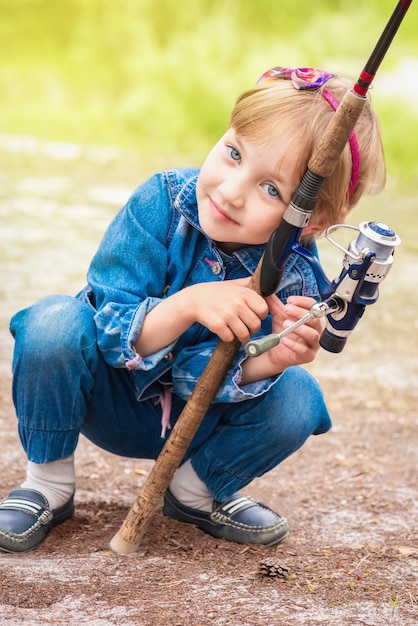 Il bambino sveglio è seduto e tiene la canna da pesca nelle sue mani.