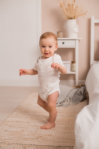 Il bambino sveglio impara a camminare la finestra del letto a casa. Primi passi del neonato che impara a camminare nella camera da letto soleggiata bianca. Interno della scuola materna