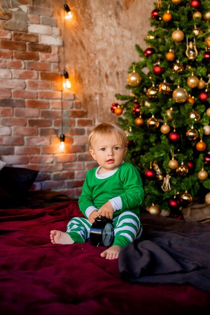 Il bambino sveglio in pigiama si siede vicino all'albero di Natale