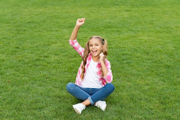 Il bambino teenager felice si siede sulla felicità all'aperto dell'erba verde