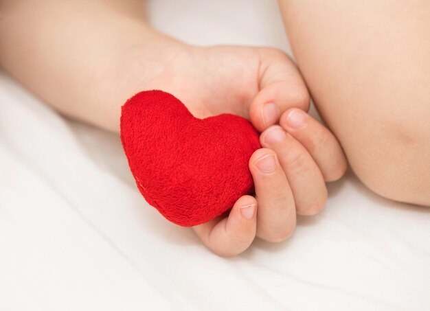 Il bambino tiene il cuore di peluche rosso. Avvicinamento