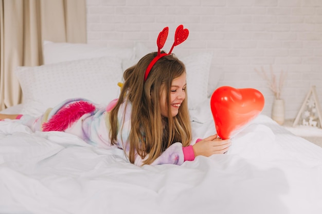 Il bambino tiene in mano un palloncino a forma di cuore. una bambina giace sul letto e tiene un cuore. San Valentino