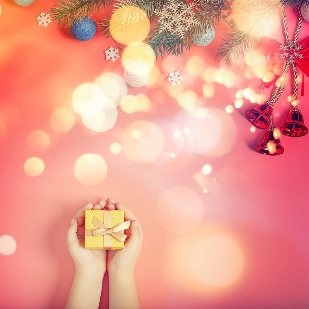 Il bambino tiene in mano un regalo di Capodanno su uno sfondo rosa con decorazioni di Capodanno.