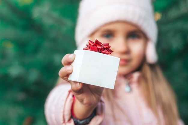 Il bambino tiene in mano un regalo per Natale una scatola bianca con un fiocco rosso, dell'albero di Natale