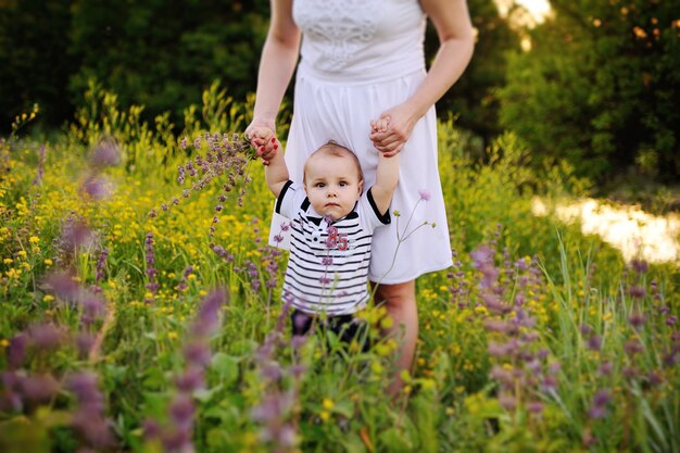 Il bambino tiene la mano della madre sulla superficie di fiori selvatici. i primi passi del bambino