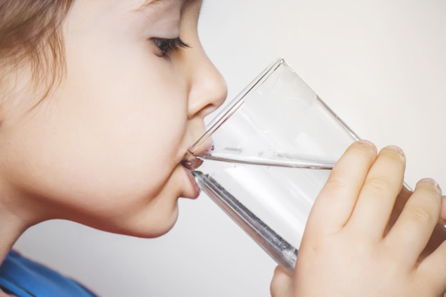 Il bambino tiene un bicchiere d&#39;acqua nelle sue mani. messa a fuoco selettiva.