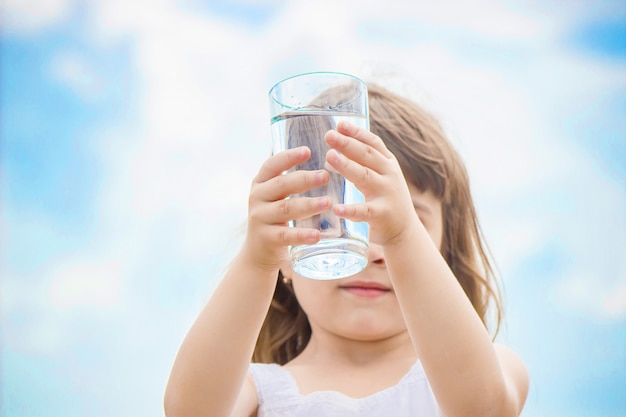 Il bambino tiene un bicchiere d&#39;acqua nelle sue mani. messa a fuoco selettiva.